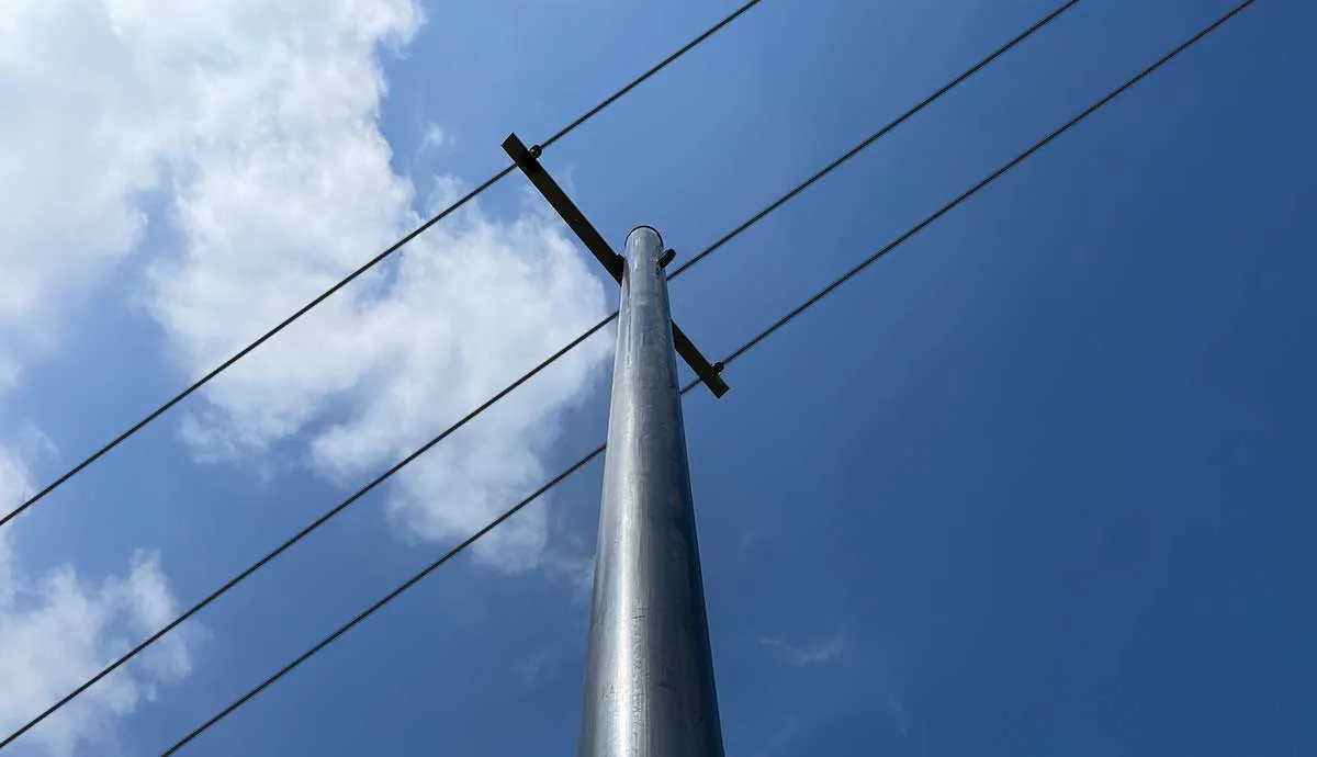 Low-angle view of a composite utility pole with three power lines against a blue sky with white clouds