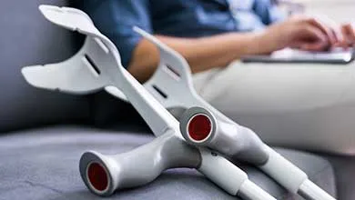 Light grey crutches lean against a couch where a person works on a laptop.