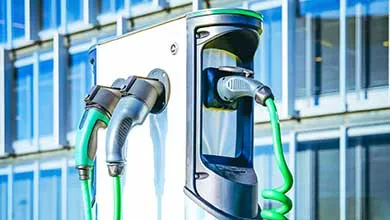 Close-up of an EV charging station with multiple nozzles and bright green cables, set against a modern glass building.