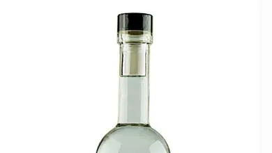 Close-up of a clear glass bottle neck, filled with clear liquid and sealed with a cork and black cap.