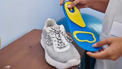 A person holds a blue and yellow insole above a gray athletic shoe on a wooden table.