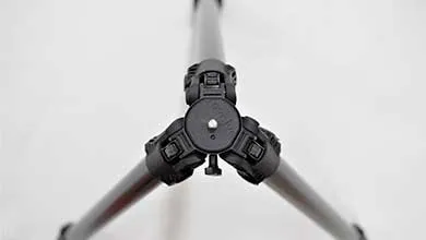 Close-up, high-angle view of a black tripod’s top where the three legs connect, on a white background.