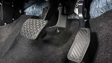 Close-up of brake and accelerator pedals in an automatic car on a dark gray carpeted floor.
