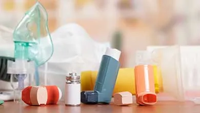 Inhalers, medical vials, and respiratory equipment arranged on a tabletop in a clinical setting.