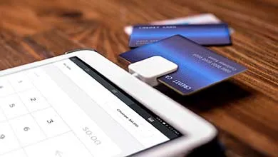 Close-up of a blue credit card in a small white card reader connected to a tablet on a wooden table.