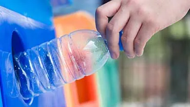Hand inserting an empty plastic bottle into a recycling bin opening.